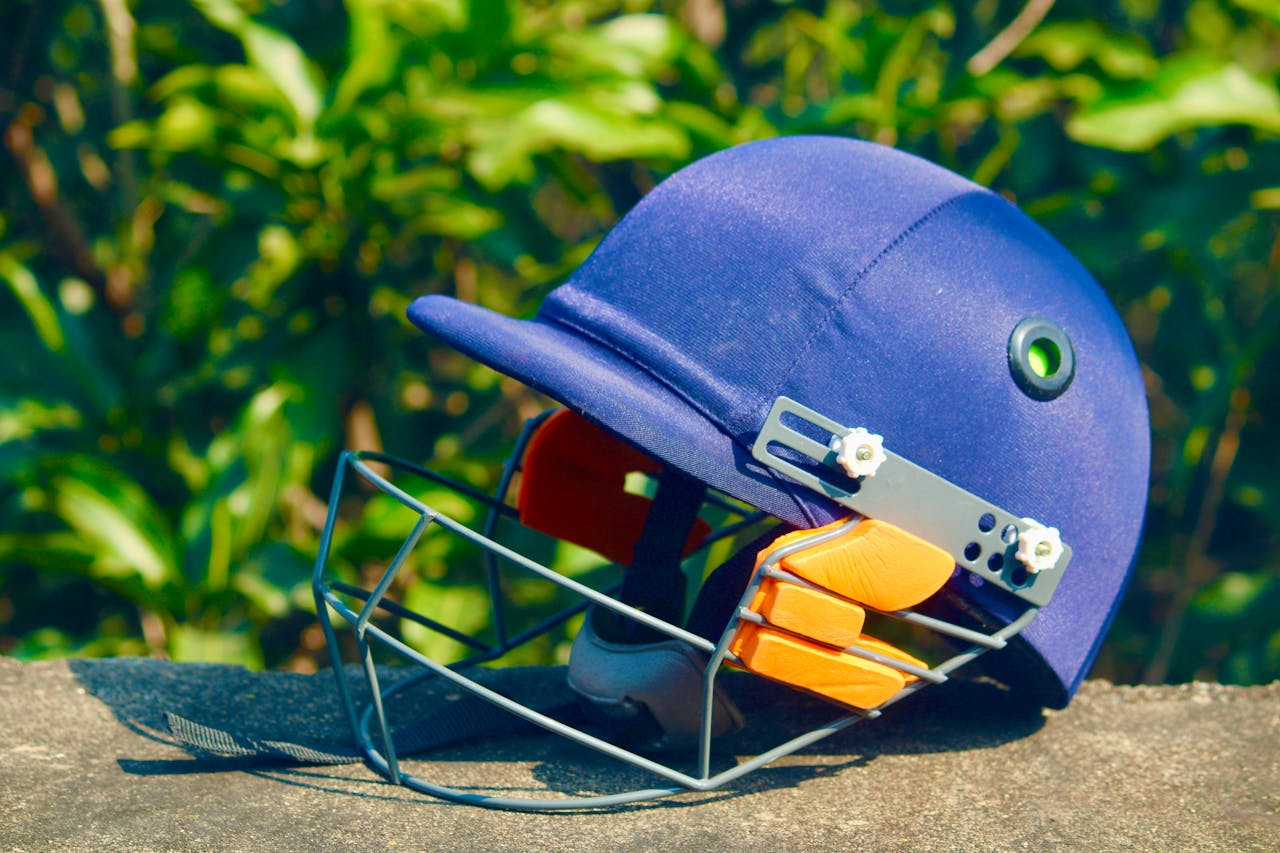 Vibrant blue cricket helmet placed on a stone surface with green foliage background, shot outdoors.